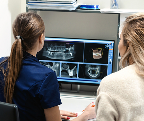 Two women looking at a computer showing x rays of a person's teeth
