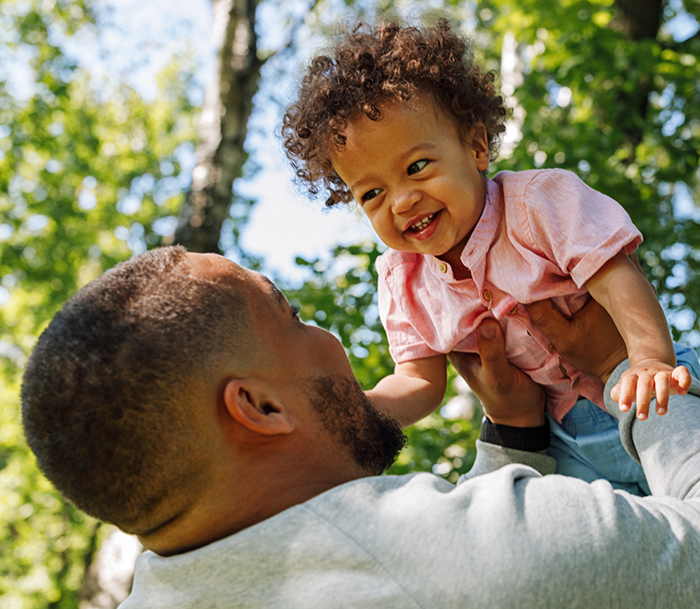 Man lifting up his toddler above his head with trees in background