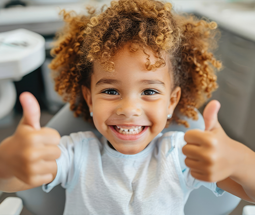 Smiling child giving two thumbs up in the dental chair