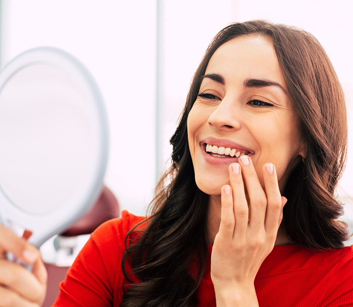 Dental patient looking at her smile in a mirror after aesthetic services in Orlando