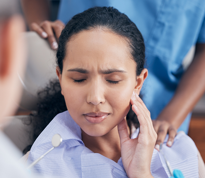 Woman holding her cheek in pain while visiting an emergency dentist in Orlando