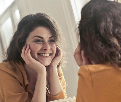 Smiling woman touching her face and looking in a mirror