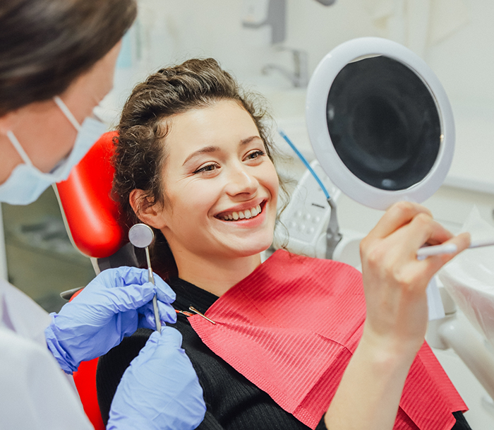 Dental patient looking at her smile in a mirror after replacing missing teeth