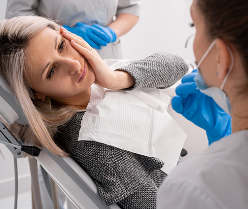 Woman holding her cheek in pain while talking to her dentist